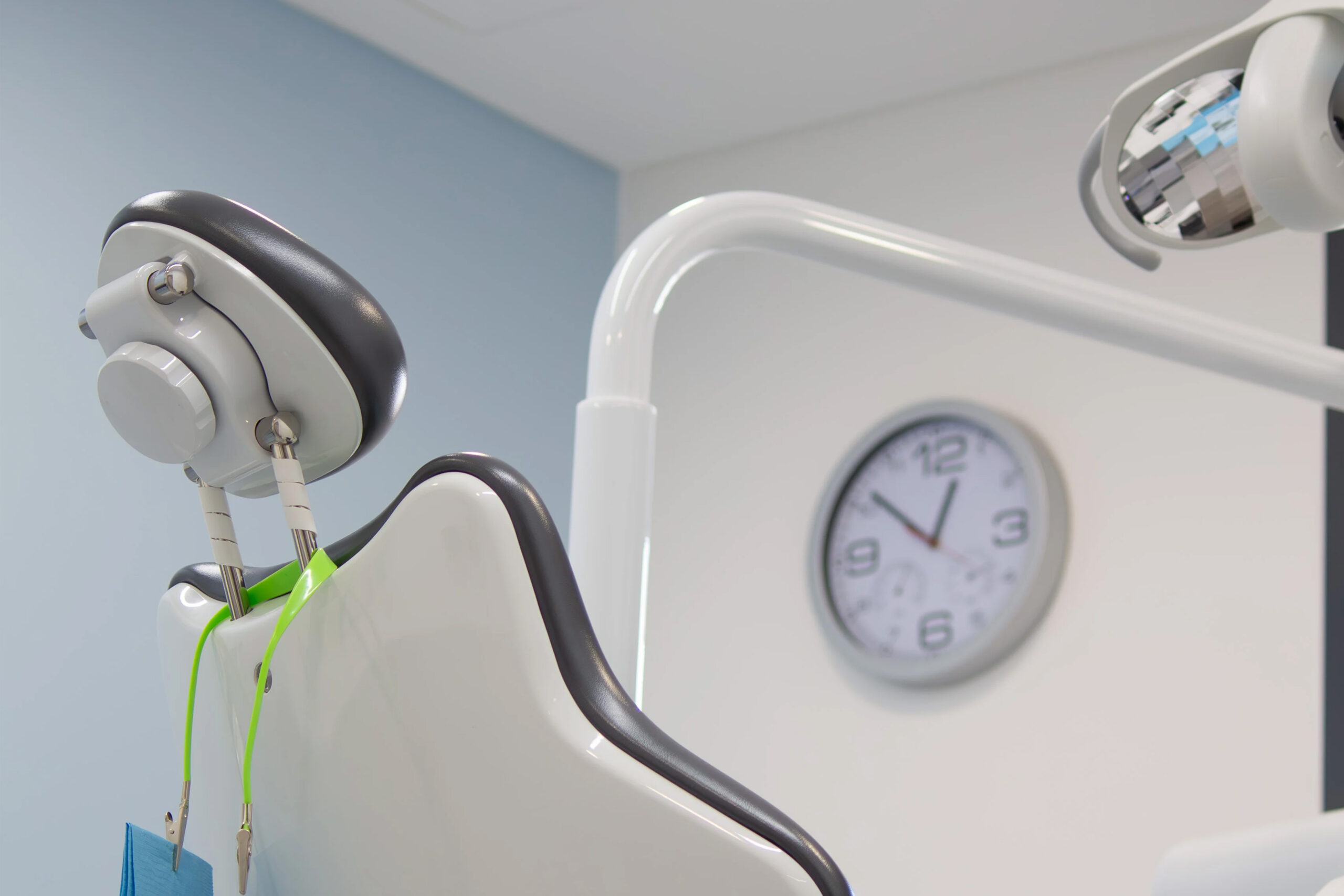 Cadeiro e iluminação de consulta dentária com um relógio ao fundo.