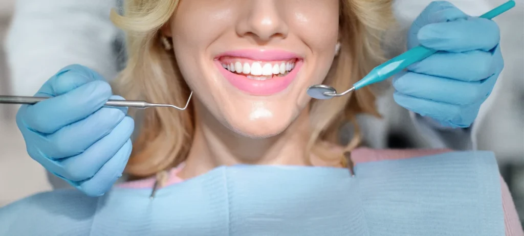 Mulher sorri durante exame dentário com instrumentos de diagnóstico.