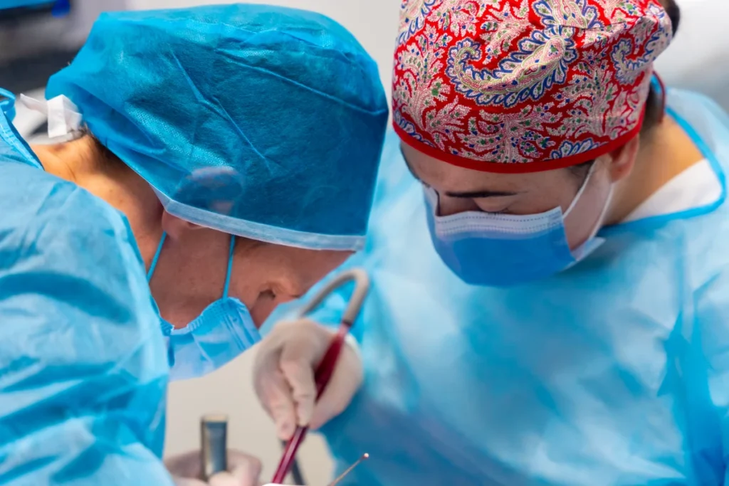 Dois profissionais de saúde em equipamento de proteção individual durante procedimento cirúrgico.