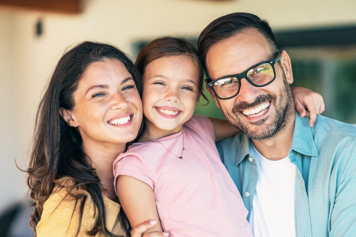 Família sorridente com uma criança no meio, abraçados e felizes.